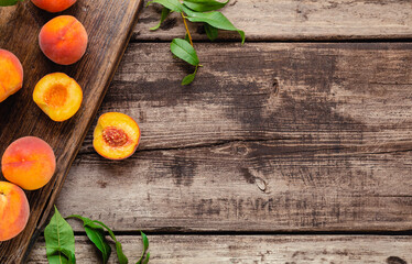Peaches with leaves on a wooden board with peach in halves. Flat lay composition with ripe juicy peaches. Harvest of peaches for food or juice. Top view fresh organic fruit food with copy space