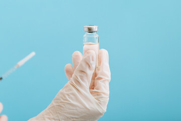 Covid 19 Vaccine in glass vial bottle and syringe, medicine liquid in doctor hand. Vaccination injections as treatment on blue background. Covid 19 Healthcare medical immunization concept.