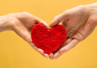 Obraz premium Heart symbol of lovers in the hands of a man and a woman on a yellow background. Valentine's Day concept.