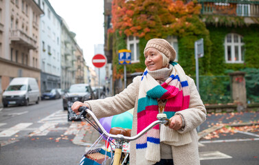 Obraz premium Senior woman with bicycle crossing road outdoors in city.