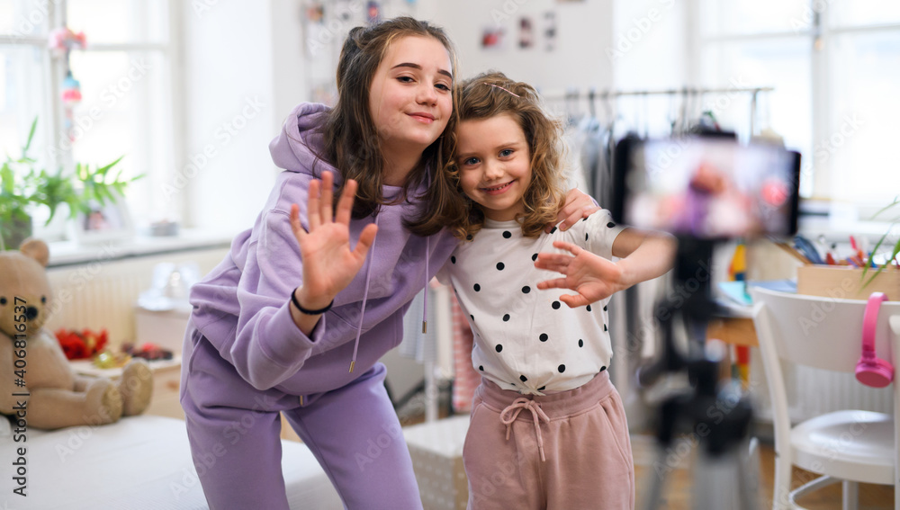 Wall mural Sisters indoors at home, making video with smartphone. Lockdown concept.