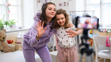 Sisters indoors at home, making video with smartphone. Lockdown concept.