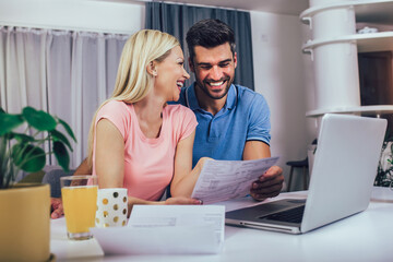 Young couple calculating budget at home. Smiling woman and man looking at laptop screen, checking...