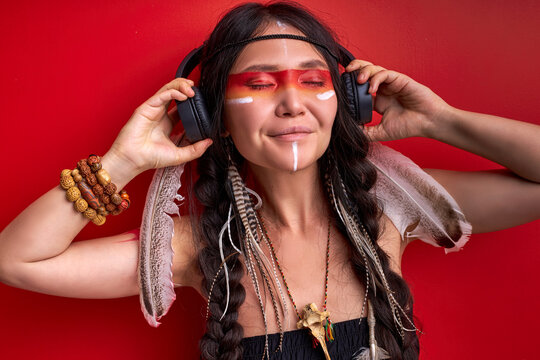 indian female using headphones, shamanic woman likes music in it, listen to music with closed eyes isolated on red background
