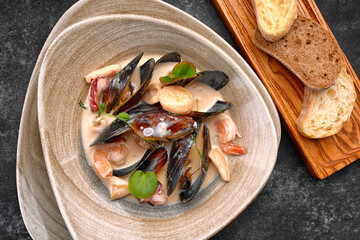 A plate of seafood, scallops, mussels, shrimps, squids, in sauce, with croutons, bread, on a wooden board