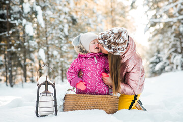 mother and daughter wrapped in a scarf in a snowy winter forest.