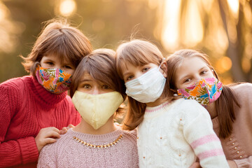 Portrait of school age children in protected face masks walk in autumn park at sunset