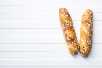 Two crispy fresh baguettes on white table.