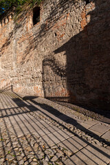 Obraz premium Detail of the shadow of a gate and of a woman with umbrella on the beautiful stone road in the medieval village of Monselice. Padua, Veneto.Italy.