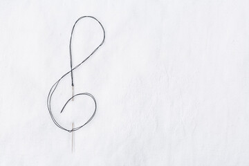 Macro of sewing needle in white fabric in violin key shape