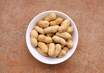 Round ceramic bowl of peanuts in shells. From above. Top view of dried peanuts in bowl. Healthy lifestyle concept. 