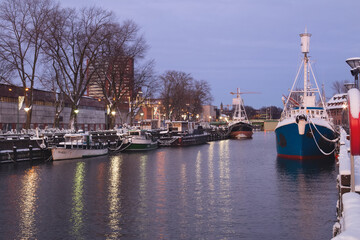 Fototapeta premium Klaipeda city, Lithuania in January. An old town, river and boats covered by winter snow, cold weather, empty streets. Beautiful red orange twilight sunset sky and street lights