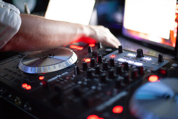 A DJ's hand reaches across his mixing table. 