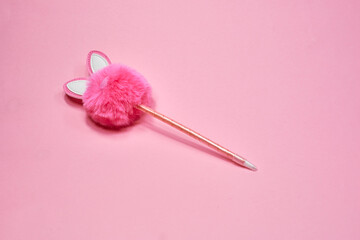 Pink fluffy rabbit in the form of a pompom and a pen on a pink background. Creative rabbit pompom...