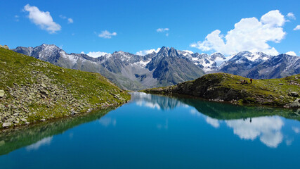 Naklejka na ściany i meble Perler See Bergsee in den Alpen, Berge mit See und blaues Wasser in Felsen mit Grün und Schnee beim Wandern für eine Auszeit und Erholung bei blauem Himmel