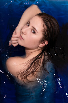 portrait of attractive brunette woman topless in blue liquid. in bathtub with colored water. drowning girl