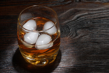 Glass of whiskey with white ice on a wooden table