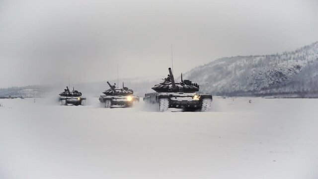 Snow-covered shooting range field in the highlands. Three tracked tanks go after each other