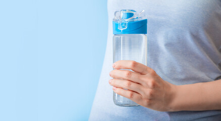 Reusable drinking water bottle for sports in female hand on blue backgraund. Healthy lifestyle and fitness concept. Long web banner with copy space