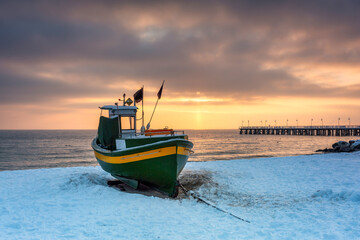 Fishing boat on snowy beach in Gdynia Orlowo at sunrise, Baltic Sea. Poland