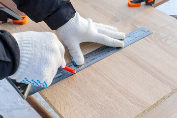 A man, a worker, marks it with a square and a pencil on a chipboard board. Draws a line.