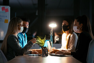 Successful concentrated business team wearing a hygienic facial mask while working together with laptops on coworking place.