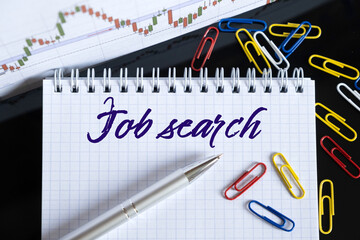 On the desktop are a forex chart, paper clips, a pen and a notebook in which it is written - Job search