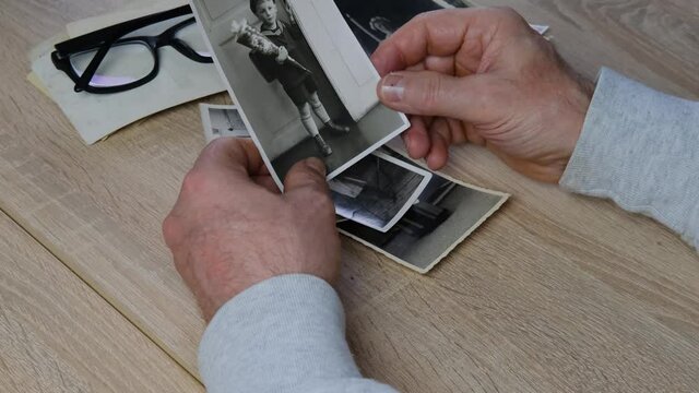 male hands fingering old photographs of 1950s, stack of old photographs on wooden table, concept of genealogy, family tree, memory of ancestors