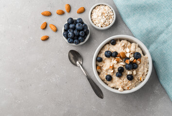 Fototapeta na wymiar Oatmeal porridge in a bowl with blueberries and almonds on grey stone background. Concept of healthy breakfast, food, and lifestyle