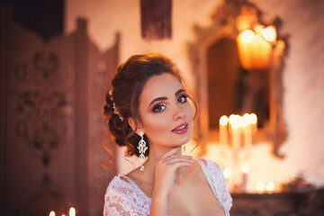 Portrait of a young beautiful girl with delicate makeup in a boudoir dress. Elegant bride's morning in a vintage loft interior with candles and roses decor.