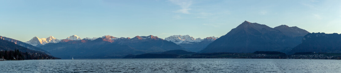 Fototapeta na wymiar Panoramic landscape at lake surrounded by mountains. Beautiful sunset light on Eiger, Monch and Jungfrau at lake thun.