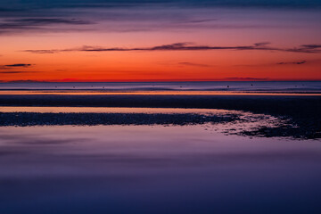 Obraz premium Purple and orange scenery at the beach just after sunset at low tide