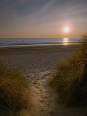 Small path between marram grass covered dunes leading towards romantic scenery prior to sunset