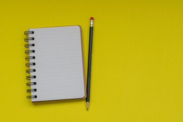 spiral notebook with white sheets and pencils on yellow background