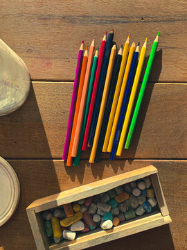 Top above overhead view of a table with a set of coloring pencils with a variety of different colors and a chalk box full of small colorful chalk pieces. Sunshine casting a shadow. Return to school.