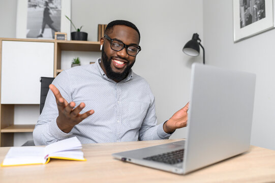 An intelligent young African-American teacher greets students at the online conference, online class on the laptop, wearing glasses, making notes. Smiling businessman on a video-call with clients