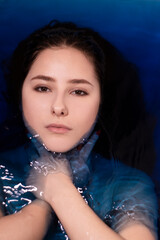 portrait of attractive brunette woman topless in blue liquid. in bathtub with colored water. drowning girl