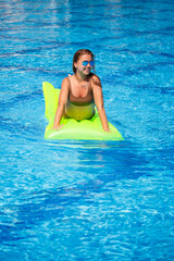 Young sexy woman in a swimsuit swims in the pool on an inflatable mattress. Girl in sunglasses with a smile on faces in a blue pool on vacation