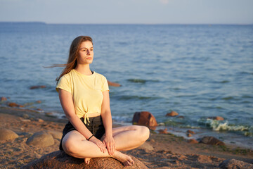 Fototapeta na wymiar Young woman sitting on the stone on the seaside. Relaxing. Slowing down. Digital detox. High quality photo