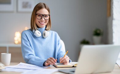 Young freelancer using laptop and making notes