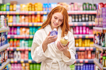 female is comparing bath salts in the household goods department, choose the best product. woman with red hair in bathrobe enjoy shopping