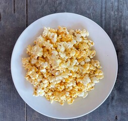 Popcorn with caramel in a white plate on a wooden background