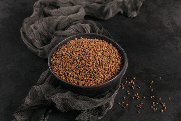 Bowl of dry raw buckwheat groats on a dark background. Cooking buckwheat porridge concept.