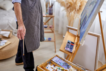 male painter man in apron during work process, male using paintbrushes, various materials paints tools for painting