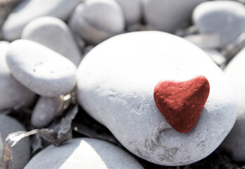 Obraz premium Red stone heart among river or sea pebble stones, Valentine's Day, perfect love