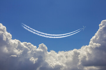 Airplane flies above white clouds in a deep blue sky and leaving jet trail in the shape of smile