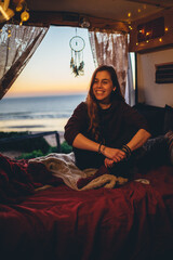 Chica pelirroja en una furgoneta camper camperizada en una zona costera de playa al atardecer leyendo y escribiendo con estilo libre hippie