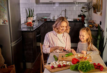 beautiful adult mother and daughter are going to prepare fresh salad together, having vegetables. food, family concept