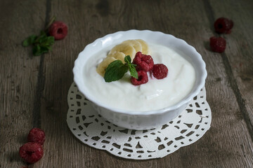 Natural homemade yoghurt in a bowl with banana slices and raspberries. Healthy breakfast with Greek yogurt