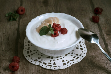 Natural homemade yoghurt in a bowl with banana slices and raspberries. Healthy breakfast with Greek yogurt